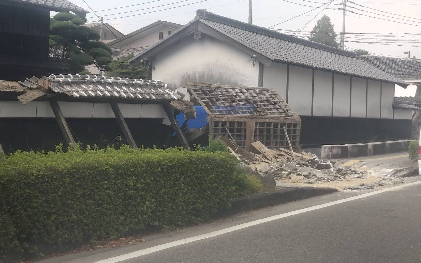 屋根と塀が崩れ、瓦礫が道路際まで散乱した住宅