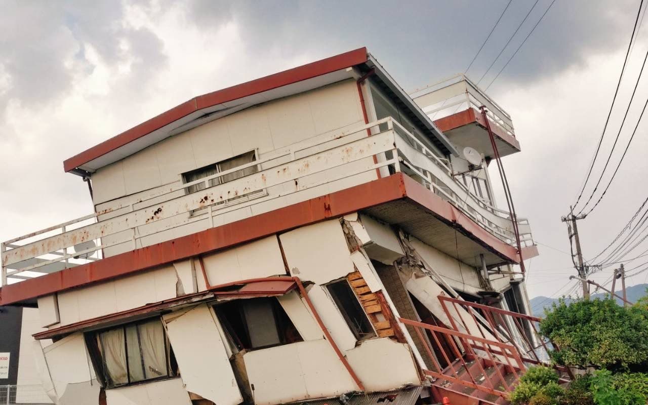 一階部分が押し潰され、大きく傾いた二階建ての建物